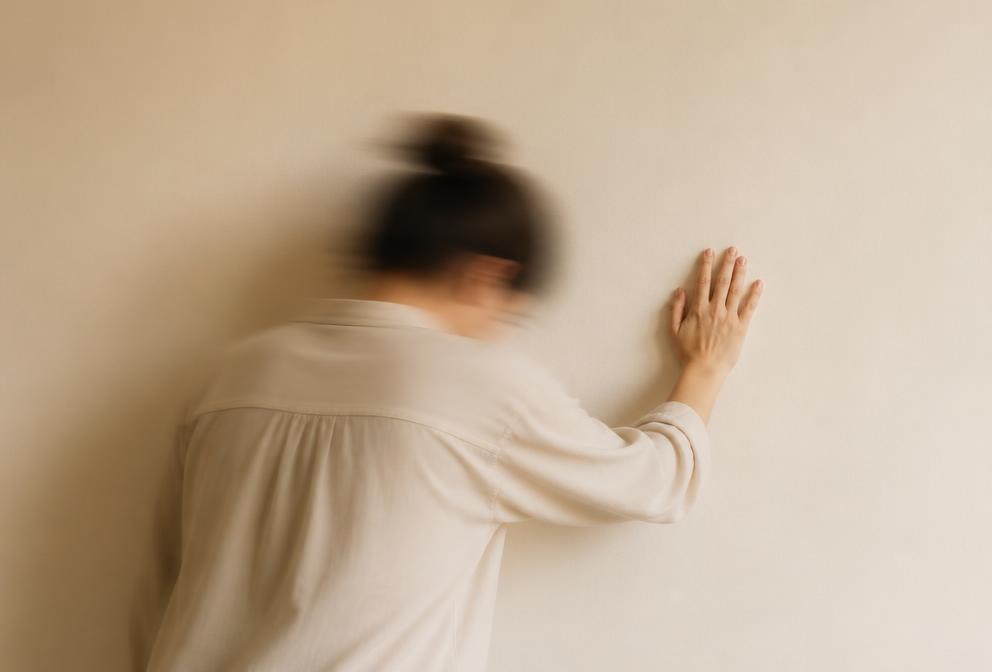 Pessoa apoiando a mão na parede para se firmar, com leve borrão de movimento
